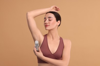 Beautiful woman applying deodorant on beige background