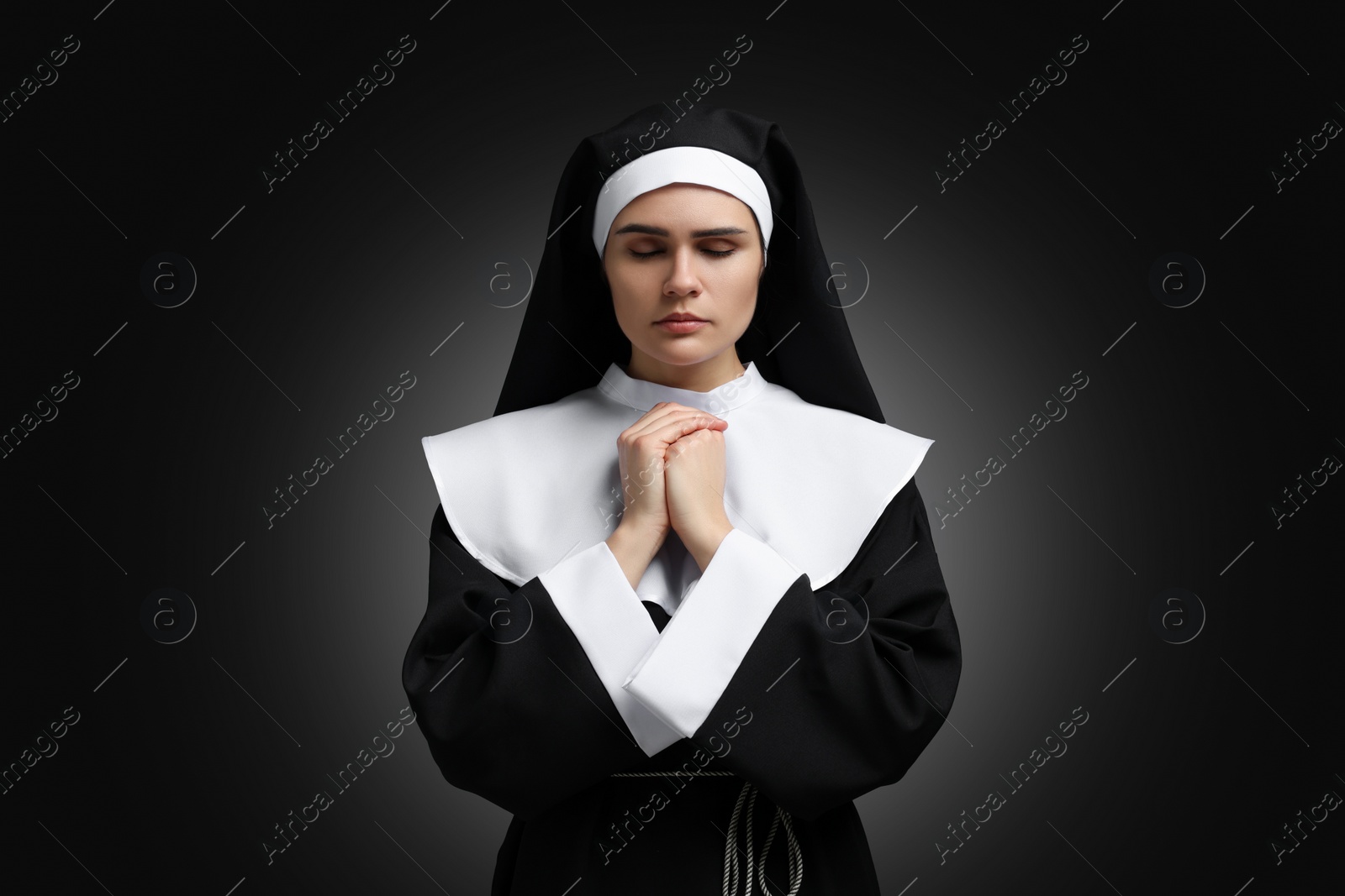 Photo of Nun with clasped hands praying to God on black background