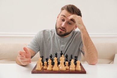 Photo of Thoughtful young man playing chess at white table indoors