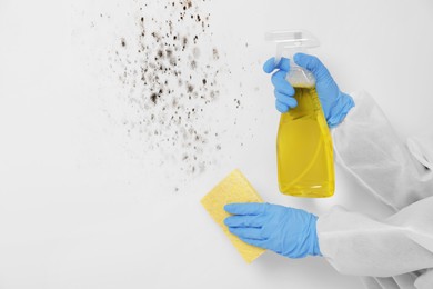 Image of Woman in protective suit and rubber gloves using mold remover and rag on wall, closeup