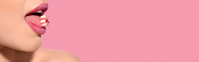 Young woman with beautiful lips holding candy on pink background, closeup view with space for text. Banner design