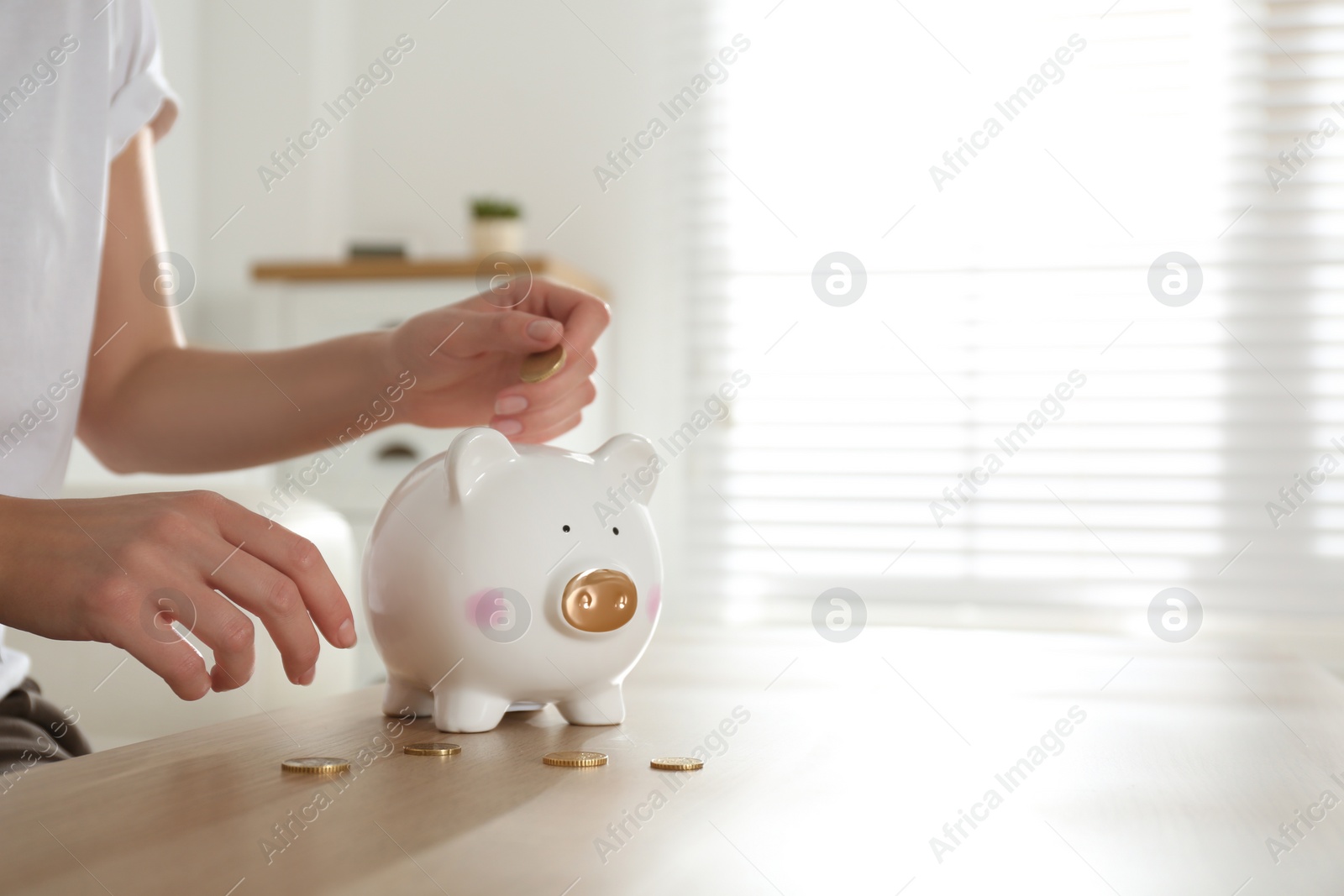 Photo of Woman putting money into piggy bank at wooden table indoors, closeup. Space for text