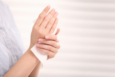 Woman cleaning hands with paper tissue on light background, closeup. Space for text