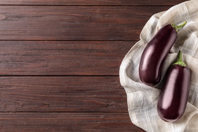 Photo of Ripe purple eggplants and napkin on wooden table, top view. Space for text