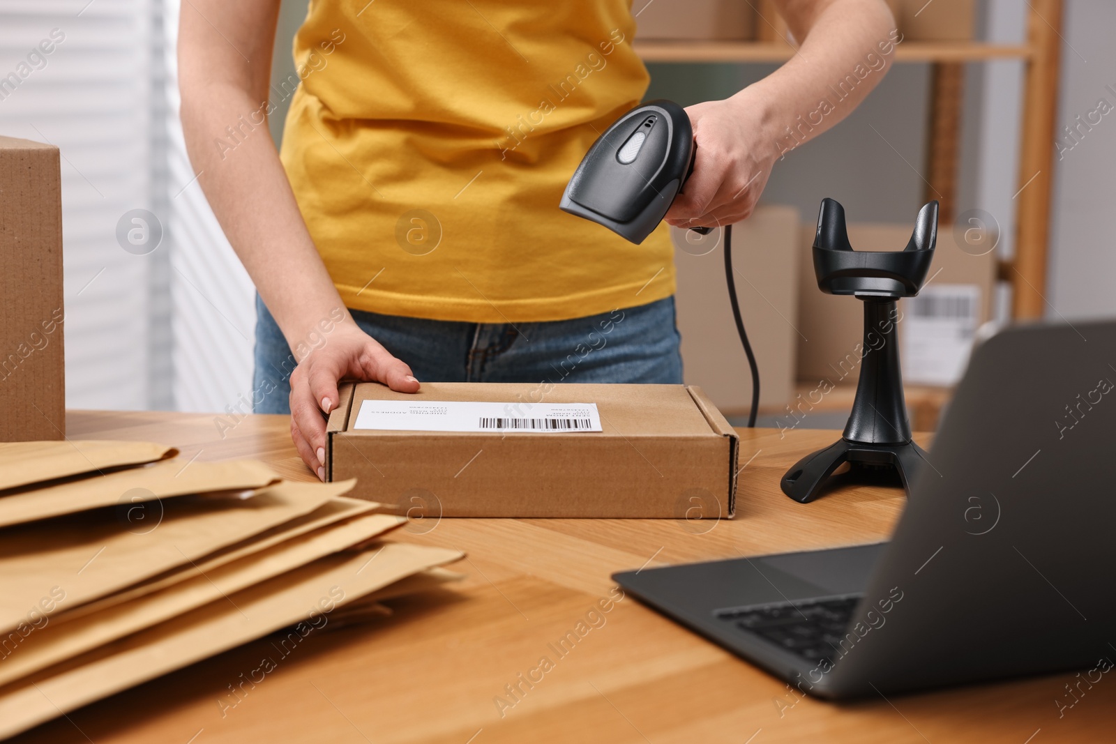 Photo of Parcel packing. Post office worker with scanner reading barcode at wooden table indoors, closeup