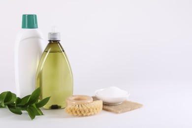 Photo of Bottles of cleaning product, brush, baking soda and green leaves on white background