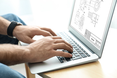 Image of Male engineer working with technical drawing on laptop at table, closeup