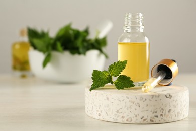 Glass bottle of nettle oil with dropper and leaves on white table, space for text