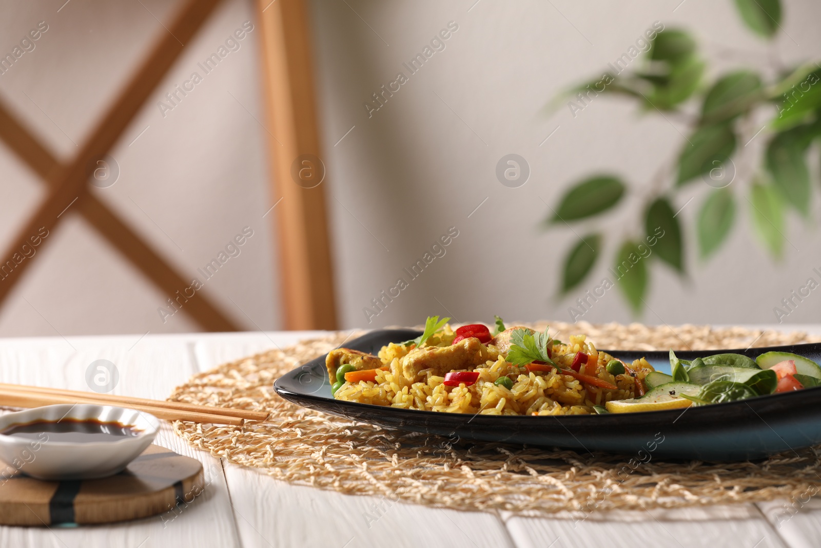Photo of Tasty rice with meat and vegetables in plate served with soy sauce on white wooden table indoors. Space for text