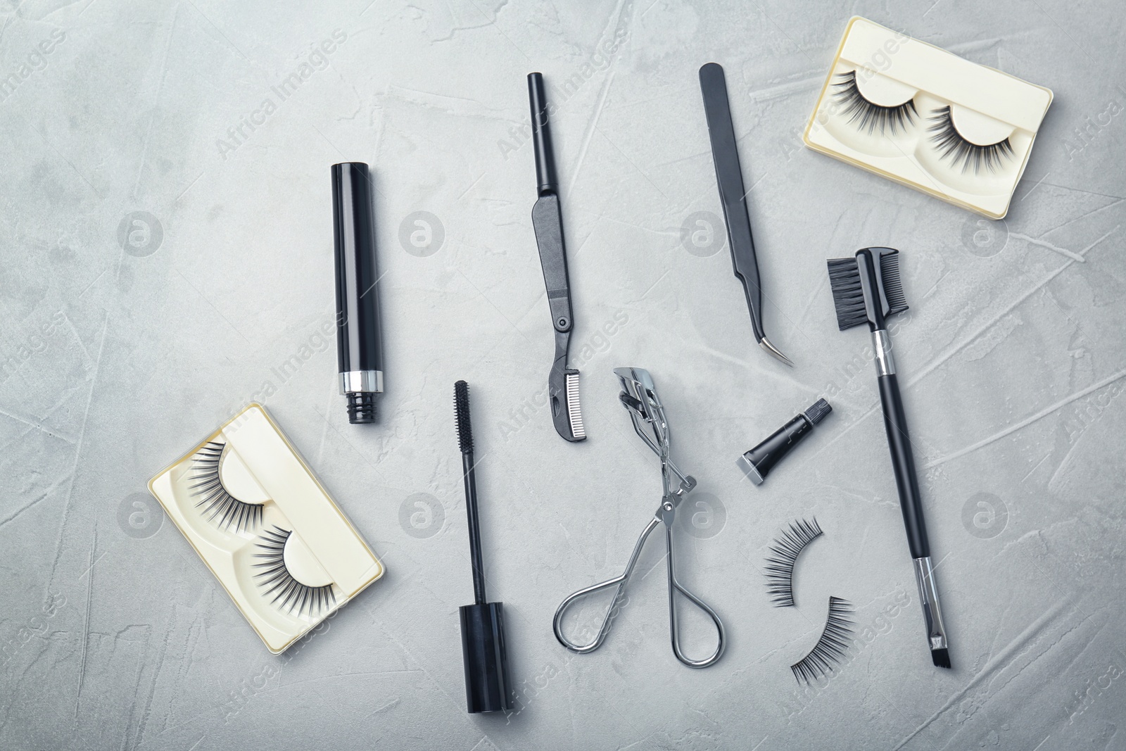 Photo of Flat lay composition with false eyelashes and cosmetic tools on grey background