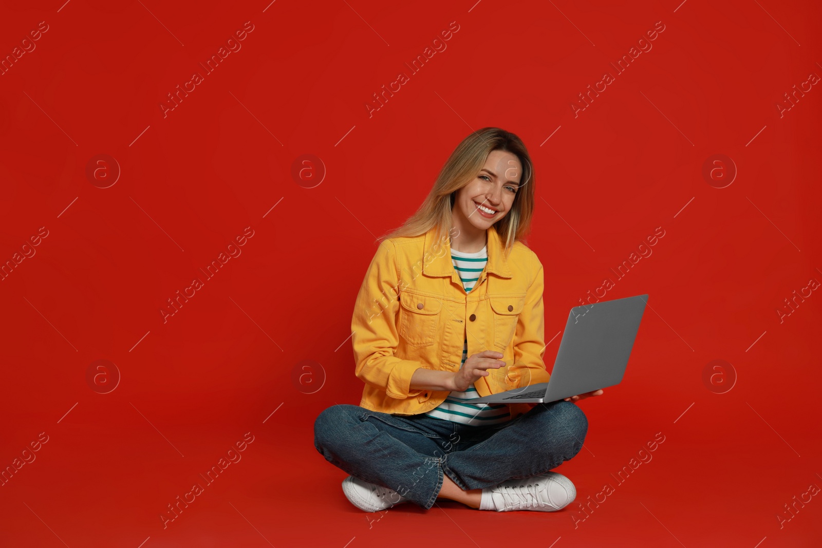 Photo of Young woman with modern laptop on red background