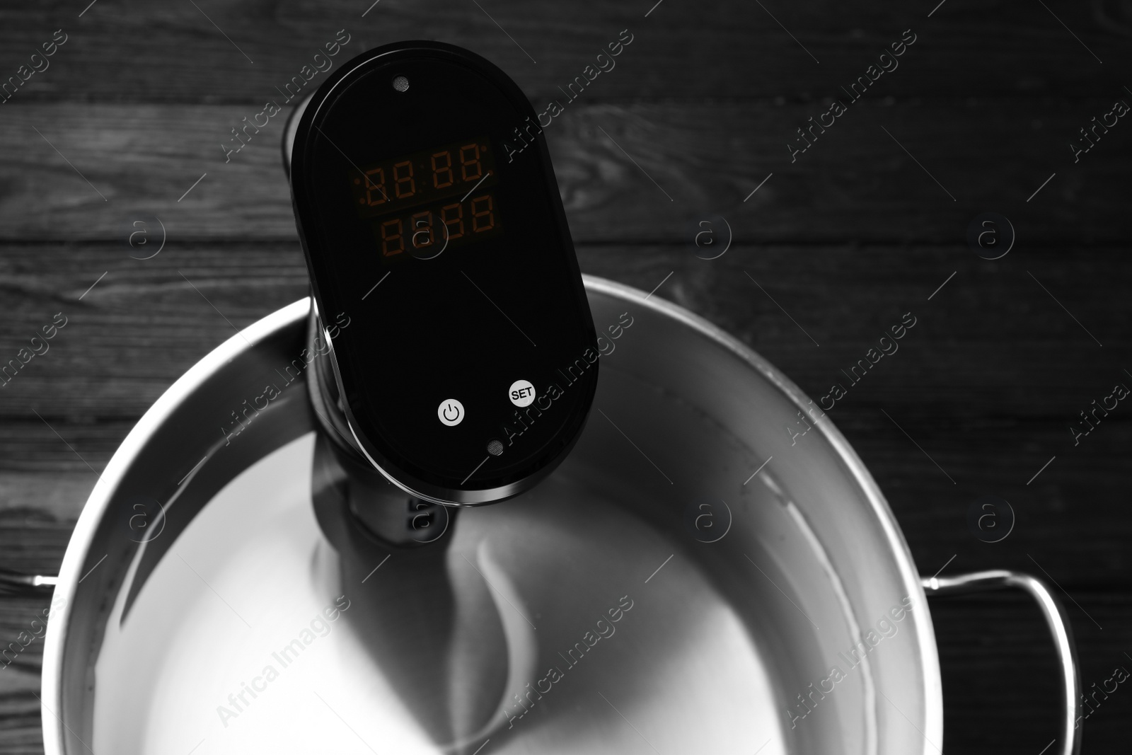 Photo of Thermal immersion circulator in pot on black wooden table, top view. Sous vide cooker