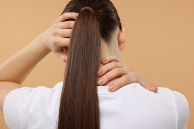 Woman touching her neck and head on beige background, back view