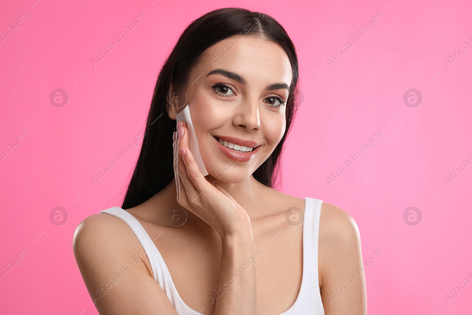 Photo of Beautiful woman using mattifying wipe on pink background