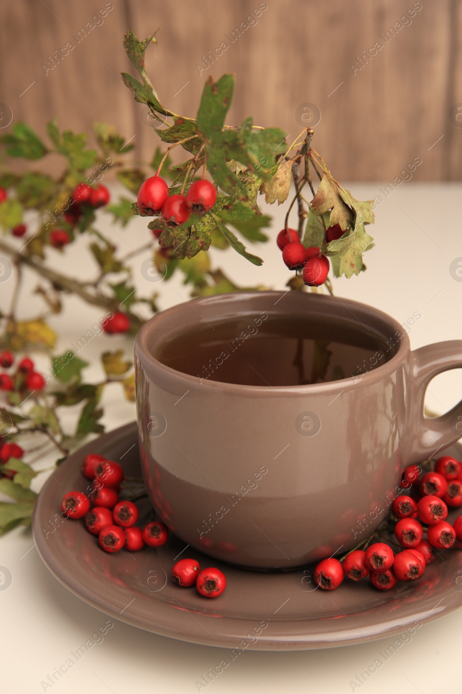 Photo of Aromatic hawthorn tea in cup and berries on beige table, closeup