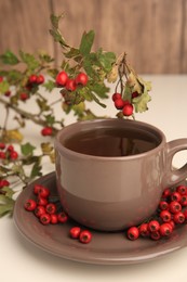 Aromatic hawthorn tea in cup and berries on beige table, closeup