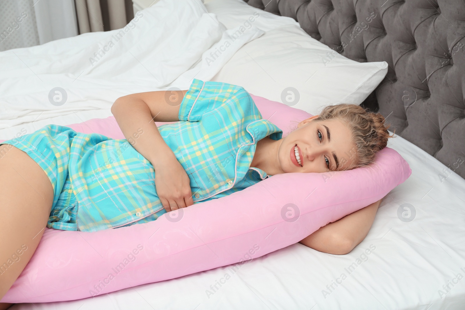 Photo of Beautiful pregnant woman lying with maternity pillow on bed at home