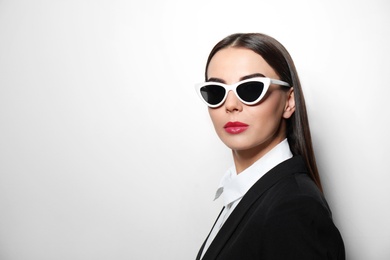 Young businesswoman in stylish sunglasses on light background, space for text