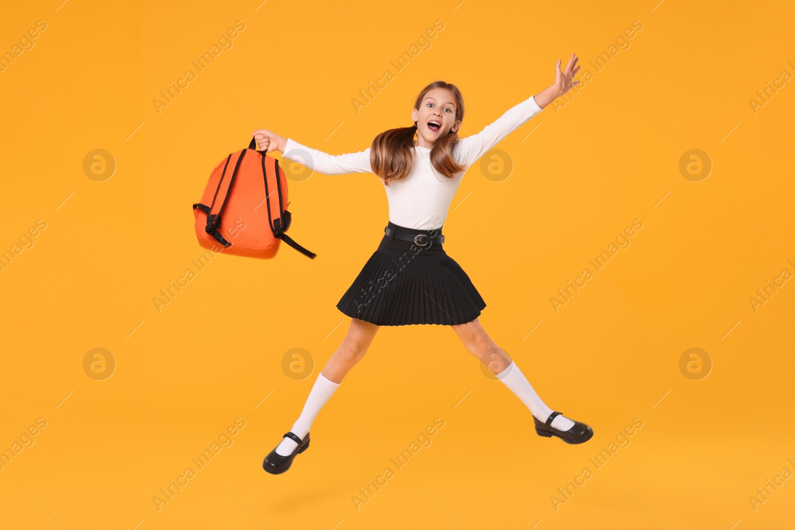 Photo of Happy schoolgirl with backpack jumping on orange background