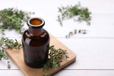 Photo of Bottle of thyme essential oil and fresh plant on white wooden table, space for text