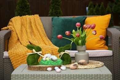 Terrace with Easter decorations. Bouquet of tulips in vase, bunny figures and decorated eggs on table outdoors