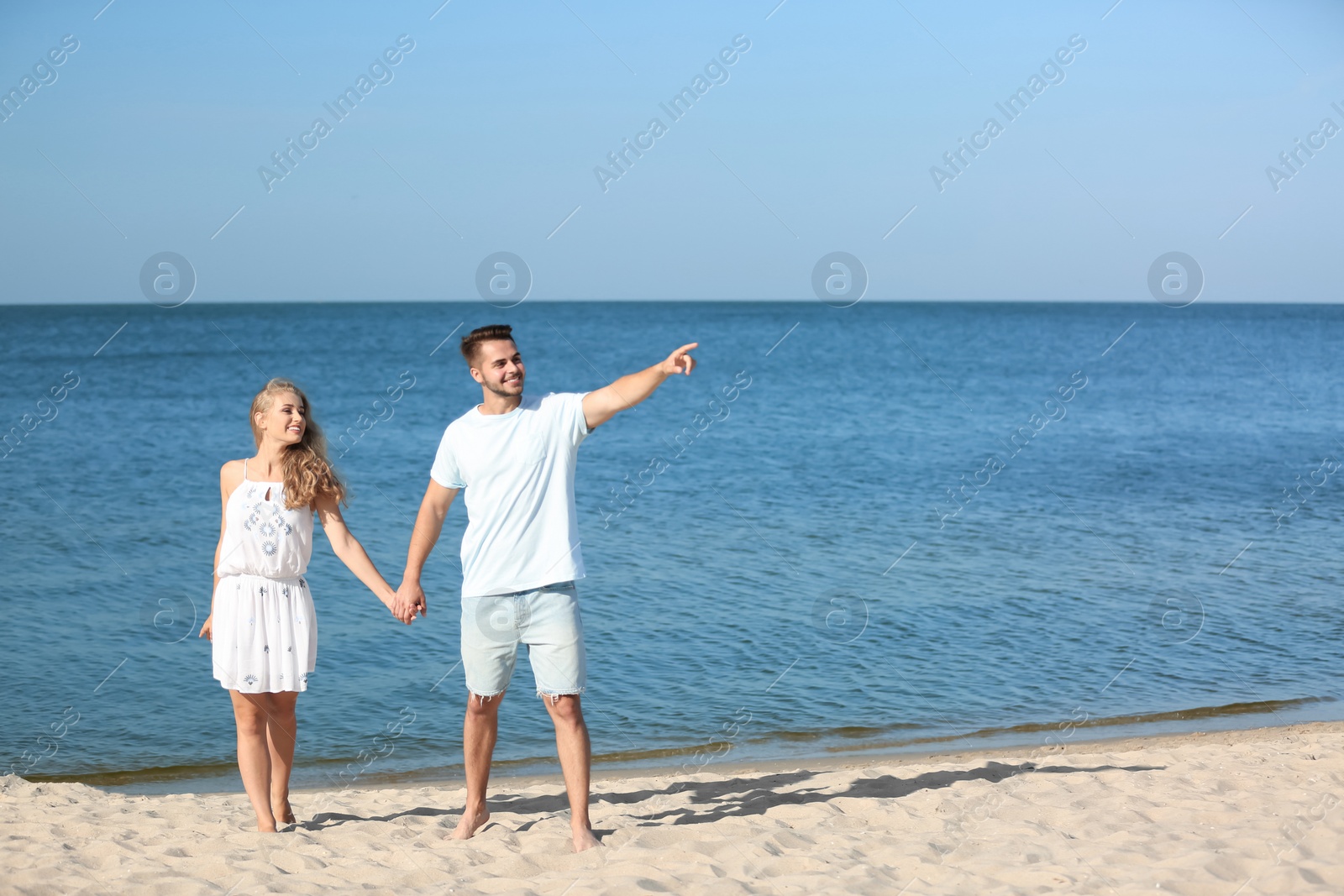 Photo of Happy young couple holding hands at beach on sunny day