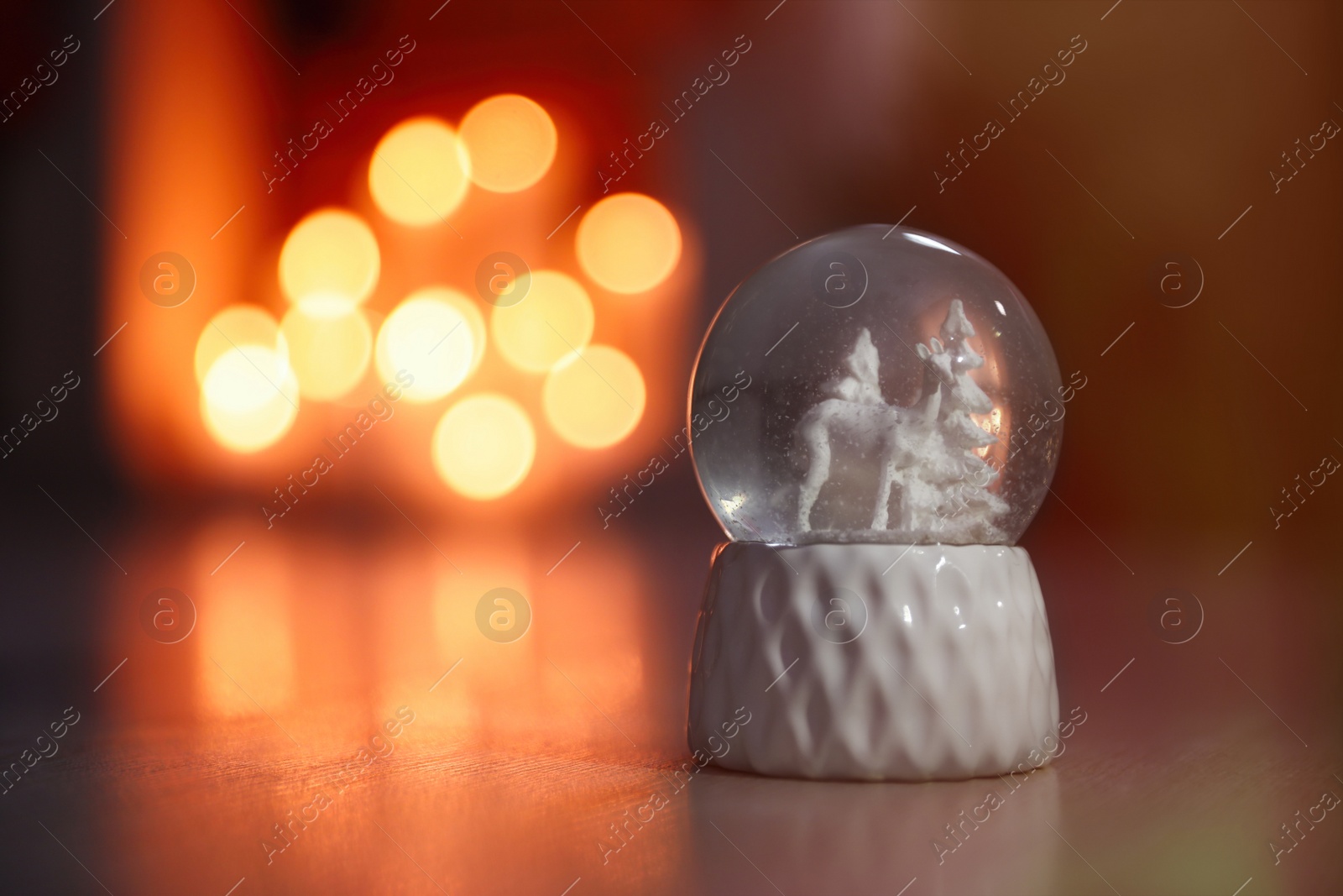 Photo of Snow globe on wooden table against blurred background, space for text. Bokeh effect