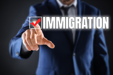 Image of Businessman touching word IMMIGRATION on virtual screen against dark grey background, closeup