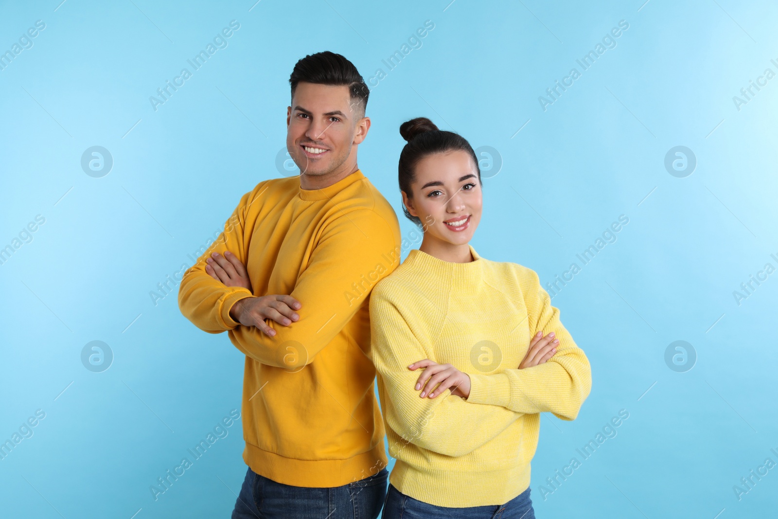 Photo of Happy couple wearing yellow warm sweaters on light blue background