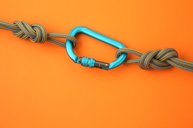 One metal carabiner with ropes on orange background, top view. Space for text