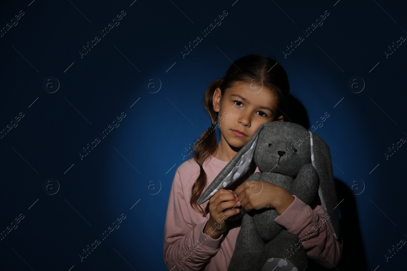 Photo of Sad little girl with toy near blue wall, space for text. Domestic violence concept