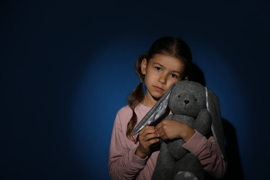 Sad little girl with toy near blue wall, space for text. Domestic violence concept