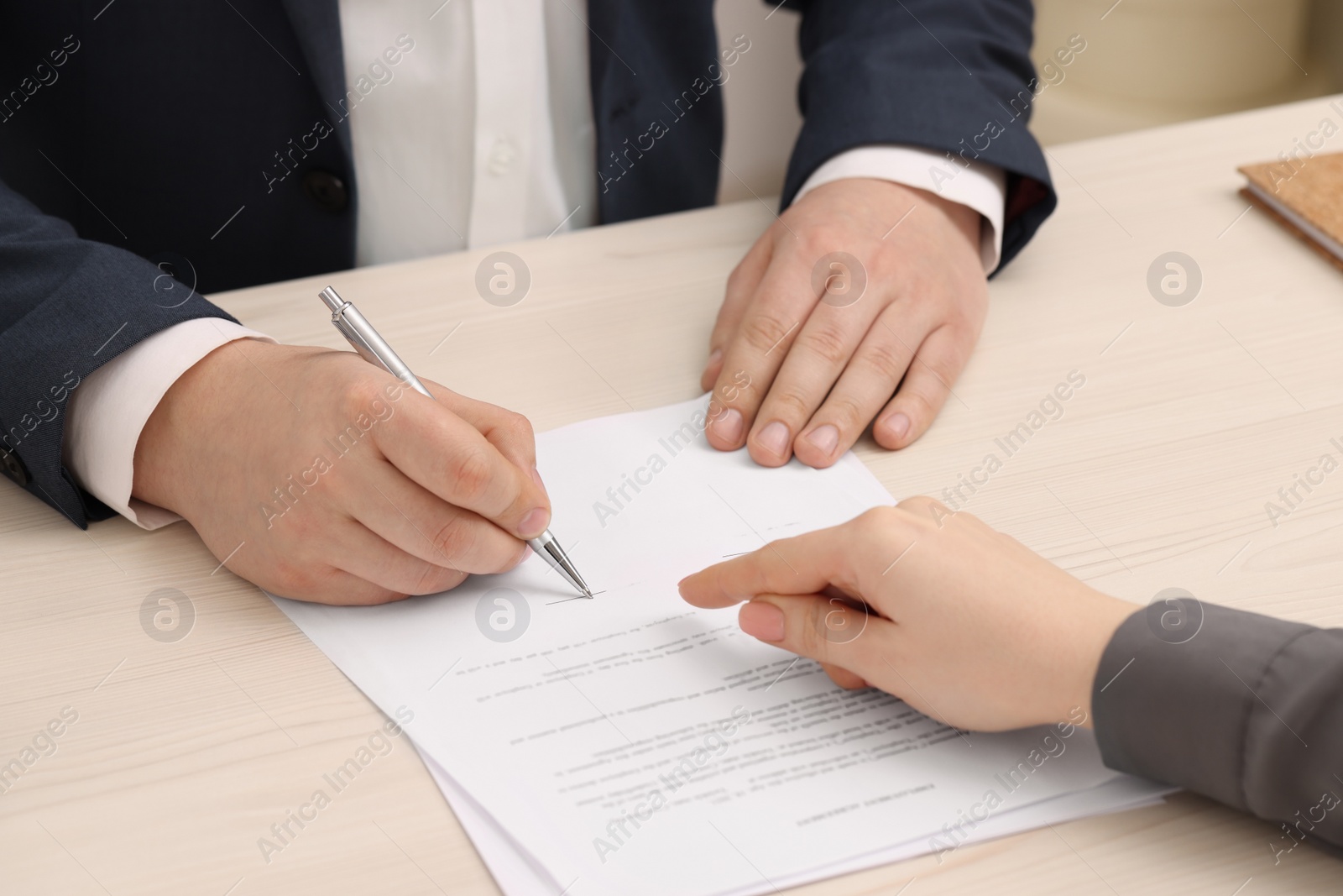 Photo of Woman pointing at document and man putting signature at wooden table, closeup