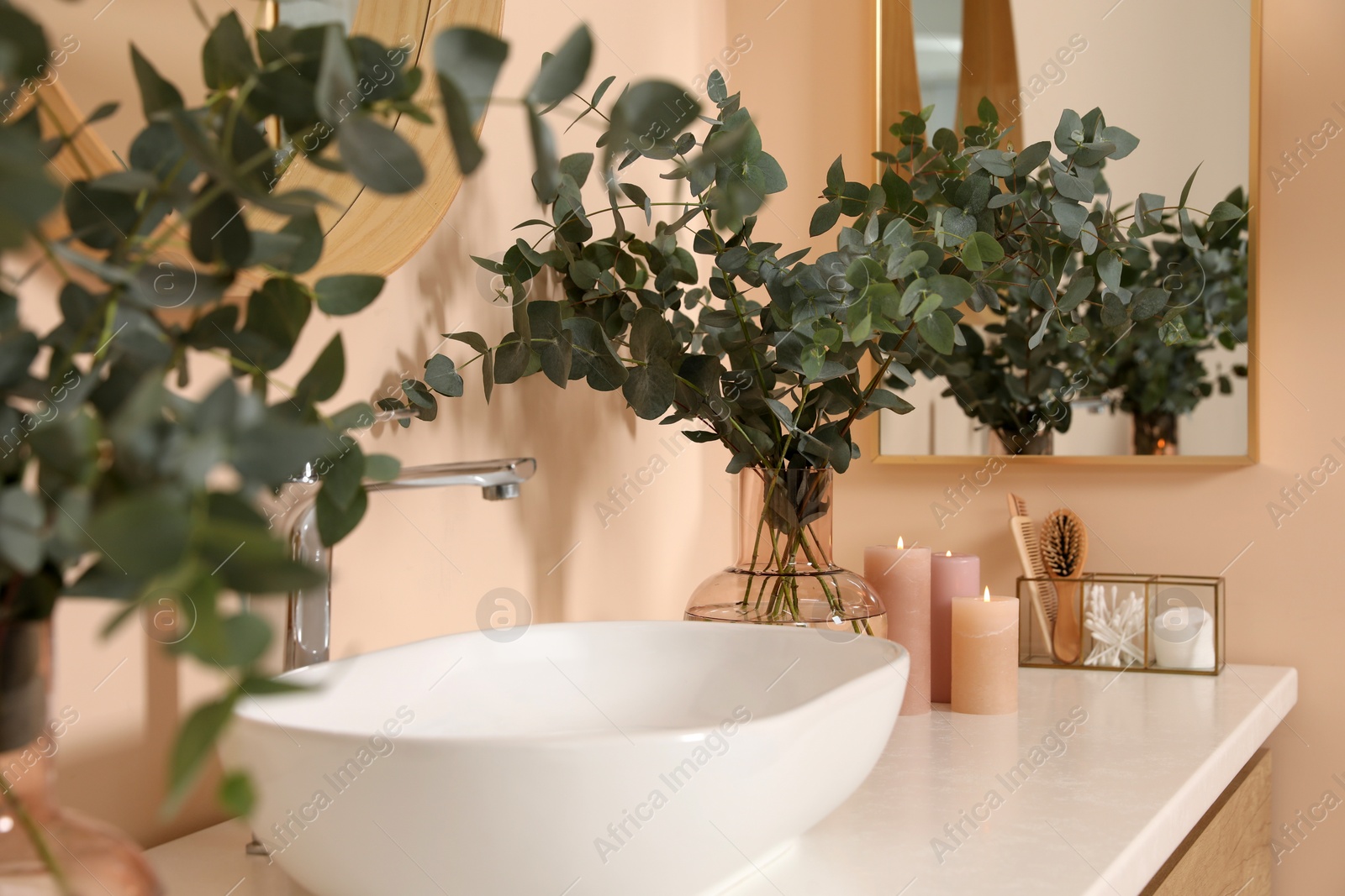 Photo of Eucalyptus branches near vessel sink on bathroom vanity. Interior design