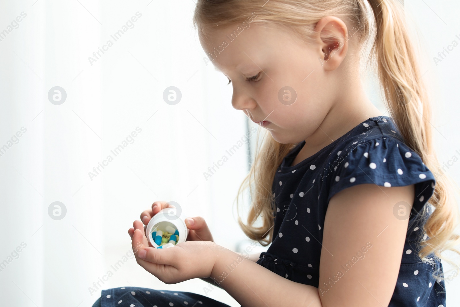 Photo of Little child with pills indoors. Danger of medicament intoxication