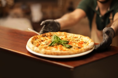 Photo of Man holding plate with oven baked pizza on table, closeup