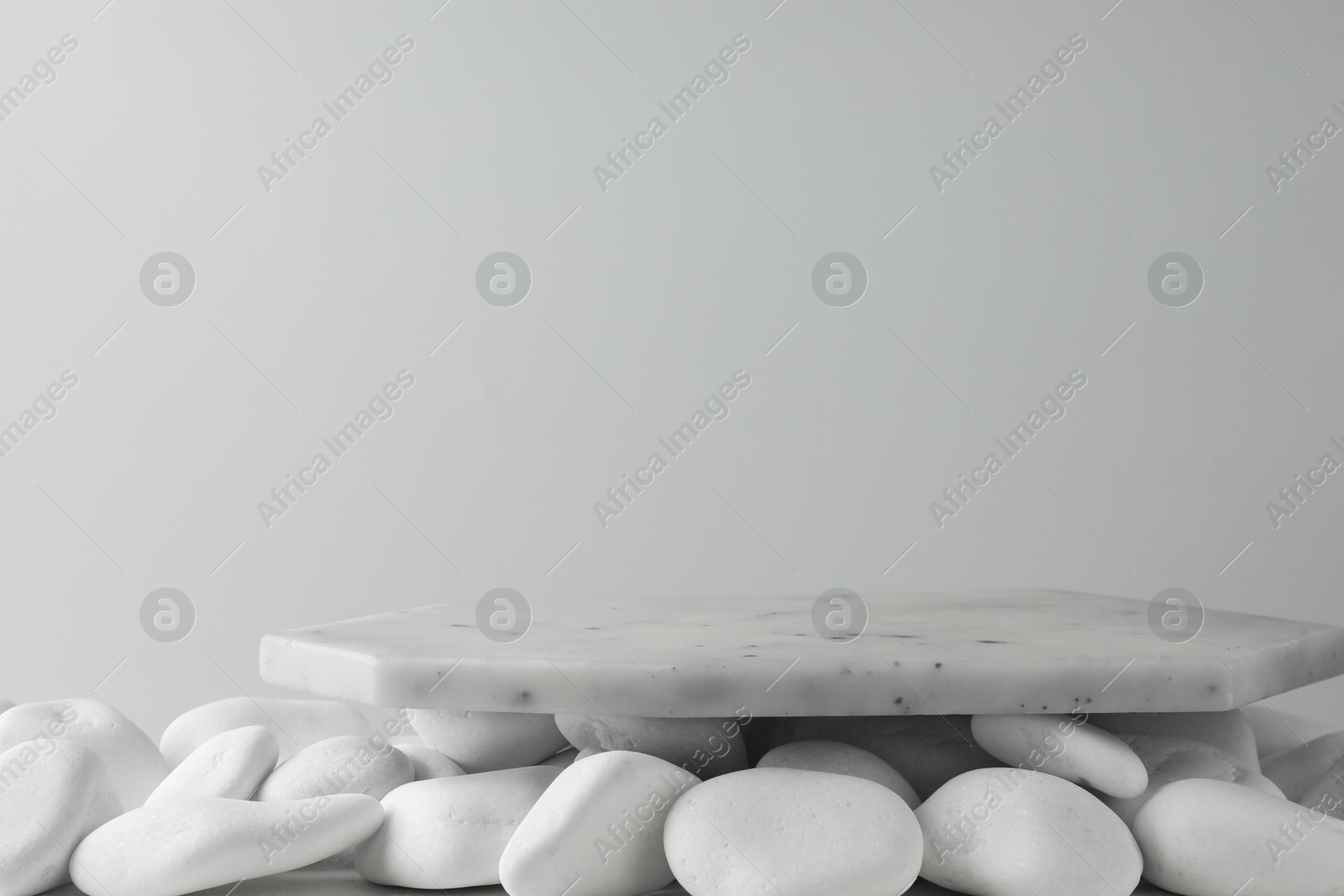 Photo of Presentation for product. Marble podium and white pebbles on light background. Space for text