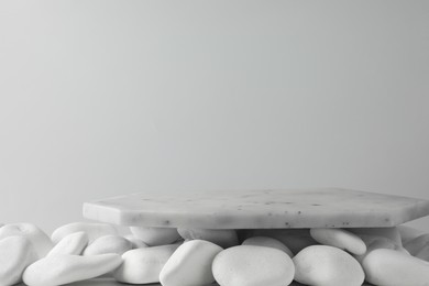 Photo of Presentation for product. Marble podium and white pebbles on light background. Space for text