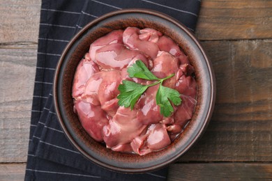Bowl with raw chicken liver and parsley on wooden table, top view