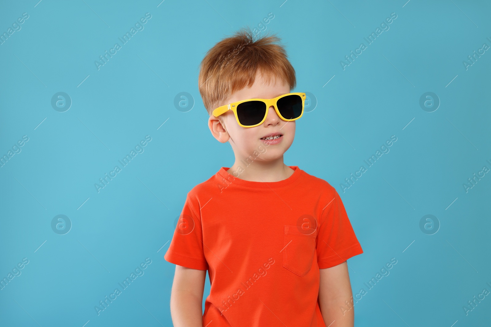 Photo of Cute little boy with sunglasses on light blue background