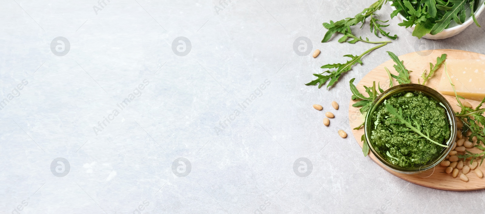 Image of Bowl of tasty arugula pesto and space for text on light table, flat lay. Banner design