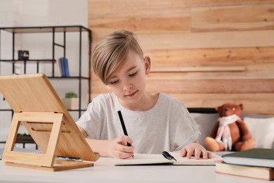 Cute boy doing homework at table indoors