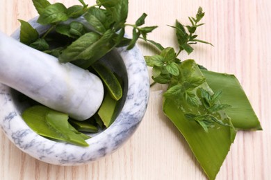 Photo of Mortar with pestle, aloe and mint leaves on wooden table, top view