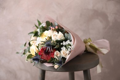 Beautiful bouquet with roses on chair near beige wall