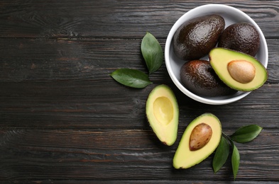 Photo of Whole and cut avocados on dark wooden table, flat lay. space for text