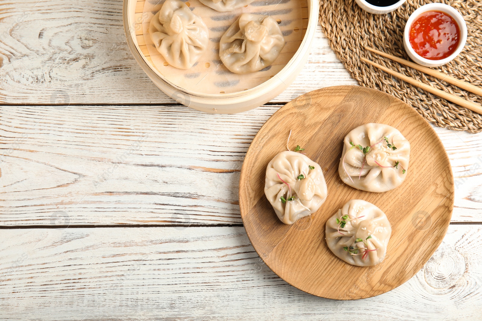 Photo of Flat lay composition with tasty baozi dumplings, bamboo steamer and sauce on white wooden table. Space for text