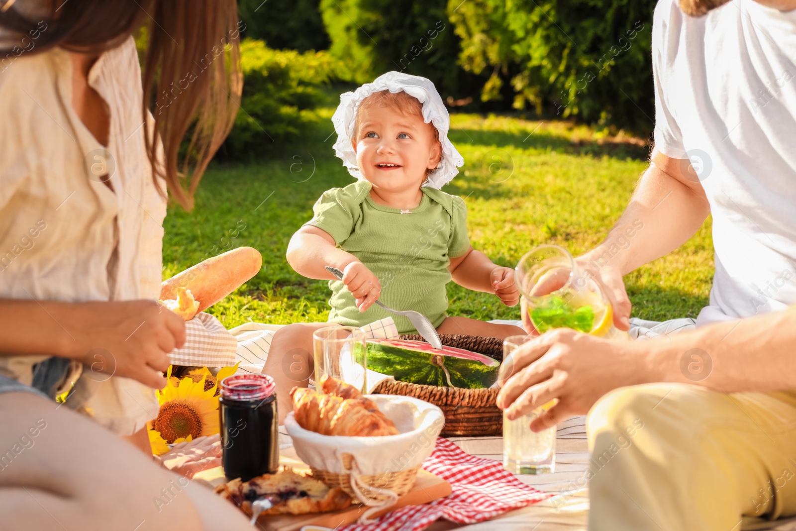 Photo of Cute child and her parents having picnic on sunny day in garden