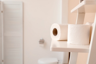 Photo of Toilet paper rolls on shelving unit in bathroom. Space for text