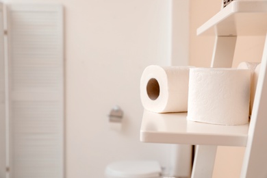 Toilet paper rolls on shelving unit in bathroom. Space for text