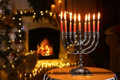 Silver menorah in dark room with fireplace and Christmas decorations, space for text